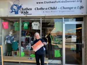 A person smiling and holding a check from Applewood in front of a Clothes to Kids of Denver store.