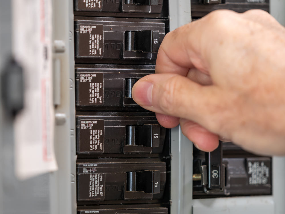 A homeowner turns off a circuit breaker in their electrical panel.
