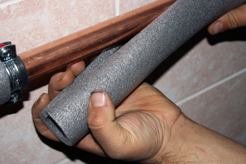 Wrapping a copper pipe in an insulated foam sleeve.