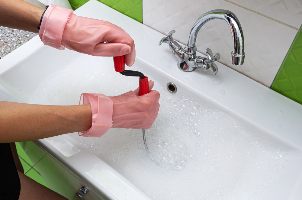 A homeowner uses a snake to unclog their bathroom sink.